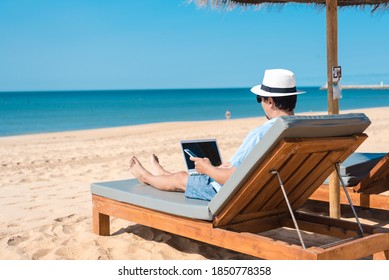 Back view of remotely telecommuting business person relaxing on the beach using tablet pc computer, dream job, education learning, teaching. Sun shining daytime natural blue sky background workplace - Shutterstock ID 1850778358