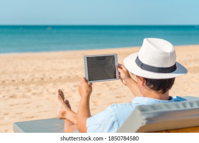 Back view of remotely telecommuting business person relaxing on the beach using tablet pc computer, dream job, education learning, teaching. Sun shining daytime natural blue sky background workplace. - Shutterstock ID 1850784580