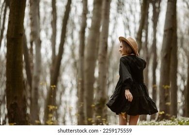Back view of romantic girl in dress walking in sunny forest. Happy woman holding hands on hat, and admiring on the landscape during stroll in amazing tranquil woods - Shutterstock ID 2259175559
