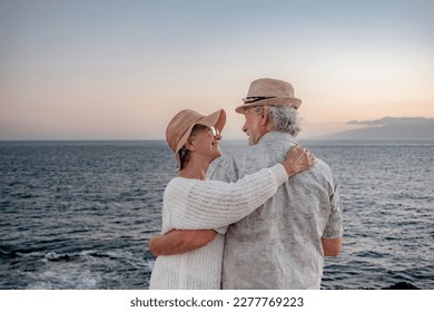 Back view of romantic senior couple or pensioners embraced at the sea at sunset light expressing love and tenderness - old couple outdoors enjoying vacations together - Powered by Shutterstock