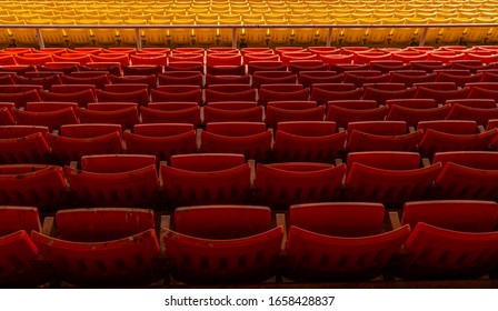 Back View Row Of Orange And Yellow Colour Folding Seats In Old Stadium Which Not Been Used For Long Time. Dirty Seats With Bird Droppings. No People In Image Of Outdoor Stadium Seats.