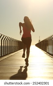 Back View Of A Runner Silhouette Running Fast At Sunset On A Bridge On The Beach