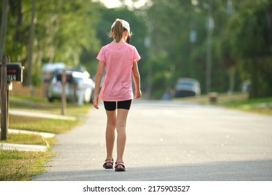 Back View Of Sad Young Child Girl Walking Alone Along The Green Street On Sunny Summer Day