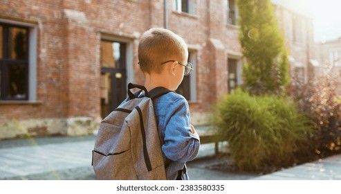 Back view. Schoolboy Little boy child with backpack alone going to school at sunset street outdoors. First-grade student primary first class education. Back to school, Happy schoolboy, Learn lessons.