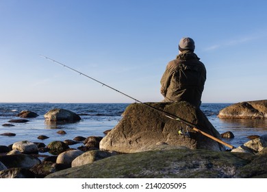 Back view of a sea trout angler with spinning rod sitting on a rock.