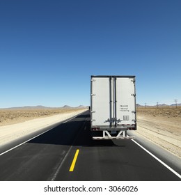 Back View Of Semi Truck Traveling Down Highway Towards Horizon Under Clear Blue Sky.