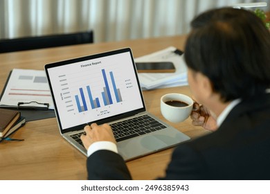 Back view of senior businessman drinking coffee and analyzing a finance report with bar chart on laptop screen. - Powered by Shutterstock