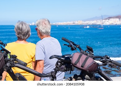 Back View Of A Senior Couple Sitting On The Cliff In Sea Excursion. Active Retirees Enjoying Healthy Lifestyle Using Bicycles - Horizon Over Water