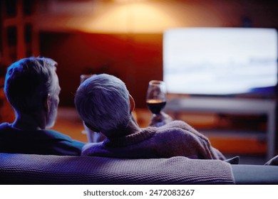 Back view of senior couple watching movie together sitting on couch at home copy space - Powered by Shutterstock