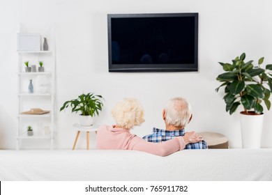 Back View Of Senior Couple Watching Tv And Embracing On Couch