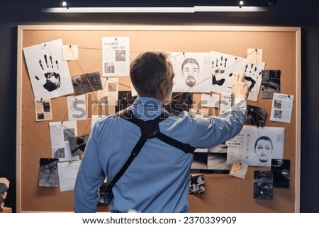 Back view of senior detective standing by evidence board and studying leads in investigation