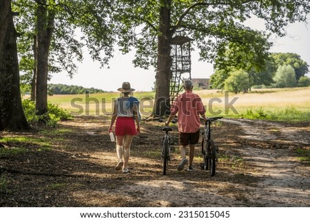 Back view of the senior father and his daughter walking with bicycles together in the park