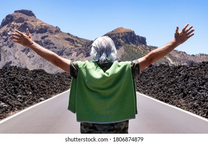 Back view of senior man in the middle of a deserted road with open arms in excursion in mountain range in Tenerife island - concept of freedom and vacation for an elderly active people - Powered by Shutterstock