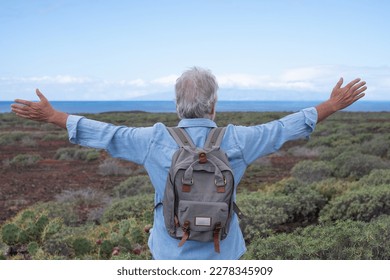 Back view of senior man with open arms in a trekking day in country footpath face to the sea, enjoying healthy lifestyle and freedom, vacation or retirement concept - Powered by Shutterstock