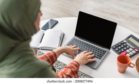 Back View Of Senior Muslim Lady Using Laptop With Empty Screen Sitting At Desk Indoor. Modern Middle-Eastern Female Browsing Internet Advertising Website. Selective Focus On Computer, Mockup