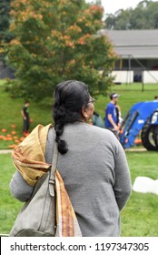 Back View Of Senior Unrecognizable Indian American Woman Enjoying A Fall Day Outside.  She's Wearing A Sweater Over Her Sari, And Walking Toward Pumpkin Patch, Hay Ride And Tree With Changing Foliage.