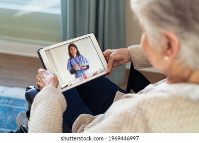 Back view of senior woman sitting in wheelchair making video call with her doctor while staying at home during covid pandemic. Sick woman in online consultation from home: distance and tele health. - Shutterstock ID 1969446997