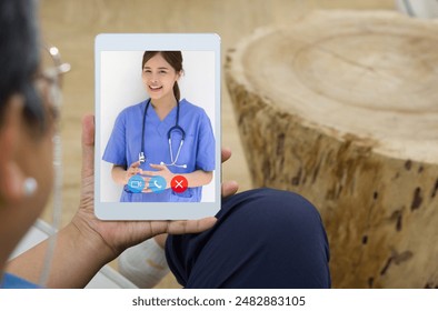 Back view of senior woman telehealth consultation on the tablet computer screen with a female doctor dressed in blue short sleeve scrub set and stethoscope. - Powered by Shutterstock