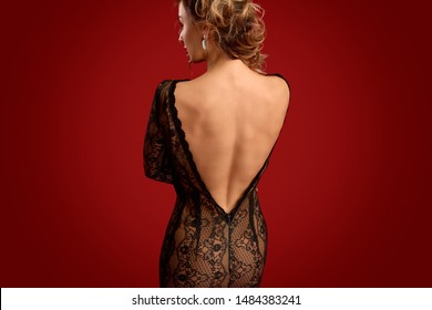 Back view of sensual female in backless lace dress looking away while standing against bright red background