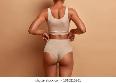 Back view of sensual slim woman poses in panties and top has perfect figure healthy dark skin isolated on brown background. Perfect female body