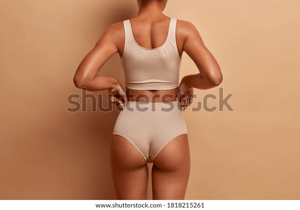 Back view of sensual slim woman poses in\
panties and top has perfect figure healthy dark skin isolated on\
brown background. Perfect female\
body