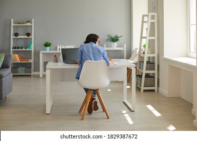 Back View Of Serious Business Lady Working On Computer In Home Office. Hard-working Businesswoman Sitting At Desk In Modern Interior Using Laptop And Taking Notes, Planning And Organizing Her Day