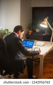 Back View Of Serious Young Man Working. Man In Suit Sitting At Laptop With Charts On Screen, Writing, Working Late. Business, Job, Occupation, Late Night Work Concept