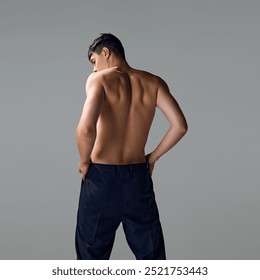 Back view of shirtless man with relief, strong, muscular body, back, posing in pants isolated on grey studio background. Concept of male beauty, body and skin care, health, sport