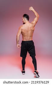 back view of shirtless man showing muscles and posing on pink and grey