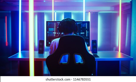 Back View Shot of the Beautiful Professional Gamer Girl Putting on Headset and Starts Playing Online Video Game on Her Personal Computer. Cute Casual Geek Girl. Room Lit by Neon Lamps in Retro Style