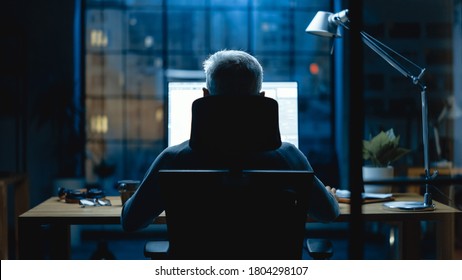 Back View Shot Of The Businessman Sitting At His Desk Using Desktop Computer. Stylish Office Studio With Dimmed Light And Big Cityscape Window View