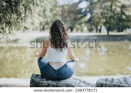 Back view shot of girl meditating sitting on a rock in the park near a lake.
