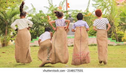 Back View Shot Of Group Of Childrens Playing Potato Sack Jumping Race Game At Park During Summer Camp - Concept Of Childhood Physical Activities And Holiday Nations.