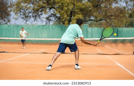 back view shot of indian senior man busy playing tennis by hitting ball with racquet at court - concept of mistakes, practising and learning - Powered by Shutterstock