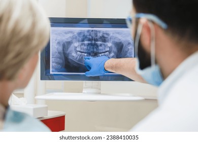 Back view shot of male dentist orthodontist showing explaining an x-ray photo of jaws on computer screen to a female patient in dental clinic. Stomatology and healthcare concept - Powered by Shutterstock