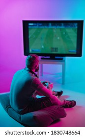 Back view shot of professional gamer playing online video game on his gameset. Room lit in neon light and retro style. Using headphones to talk with the team. Entertainment, fun concept. - Shutterstock ID 1830748664