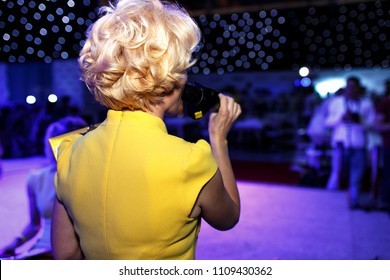 Back View Of Show Host Blonde Woman Holding Microphone Standing On Decorated Stage