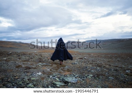 Back view silhouette of male traveler in medieval clothes. Man is walking through the mountains on the background of the dramatic cloudy sky.
