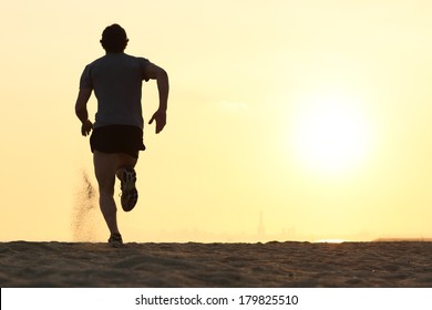 Back View Silhouette Of A Runner Man Running On The Beach At Sunset With Sun In The Background