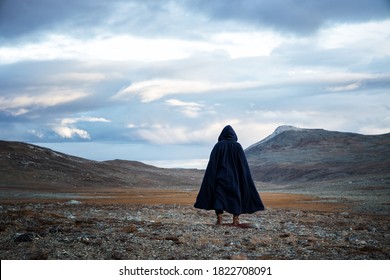 Back view silhouette of traveler man standing on the mountain.  A mysterious cloaked man. Medieval man in hooded cloak. - Shutterstock ID 1822708091