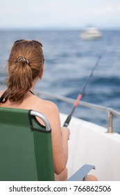 Back View Of Sitting Woman With Long Hair Hold A Fishing Rod Catching  Fish On Deep Sea Fishing Boat. 