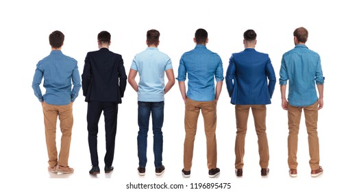 back view of six relaxed young men wearing suits and blue shirts standing on white background with hands in pockets, full length picture