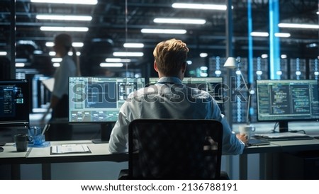 Back View of Skilled Focused System Administrator or Consultant Checks and Saves Backup Data in Dark Evening Room Workplace Station Indoors. Network Technologies Concept