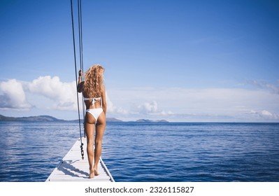 Back view of slim unrecognizable female blondie in white bikini standing on wooden pier near sea against blue sky with clouds during daytime - Powered by Shutterstock