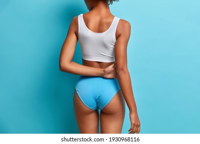 Back view of slim woman with perfect buttocks slender legs has healthy skin being in good shape wears cropped top and panties isolated over blue background