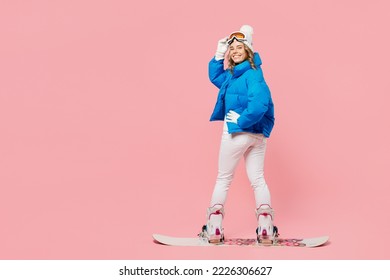 Back view snowboarder woman wear blue suit goggles mask hat ski padded jacket snowboarding look camera isolated on plain pastel pink background. Winter extreme sport hobby weekend trip relax concept