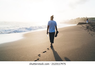 Back view of sportive man holding bottle of water and mat for stretching and walking around seashore beach during weekend morning time, Caucaisan male yogi spending leisure at sandy coastline - Powered by Shutterstock