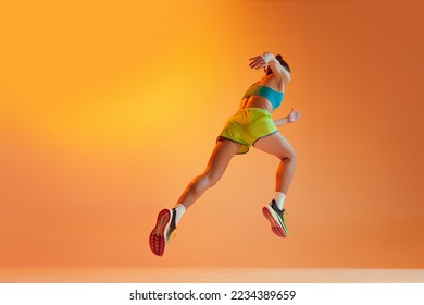 Back view. Sportive muscled woman, professional runner running away isolated on yellow background in neon light. Sport, fitness, competition, speed and active lifestyle. Copy space for ad. Sunset