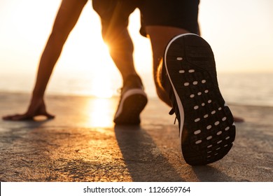 Back view of a sportsman getting ready to run at the beach in sunlight