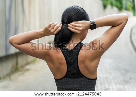 Back view of sportswoman securing her ponytail with black terry cloth hair tie